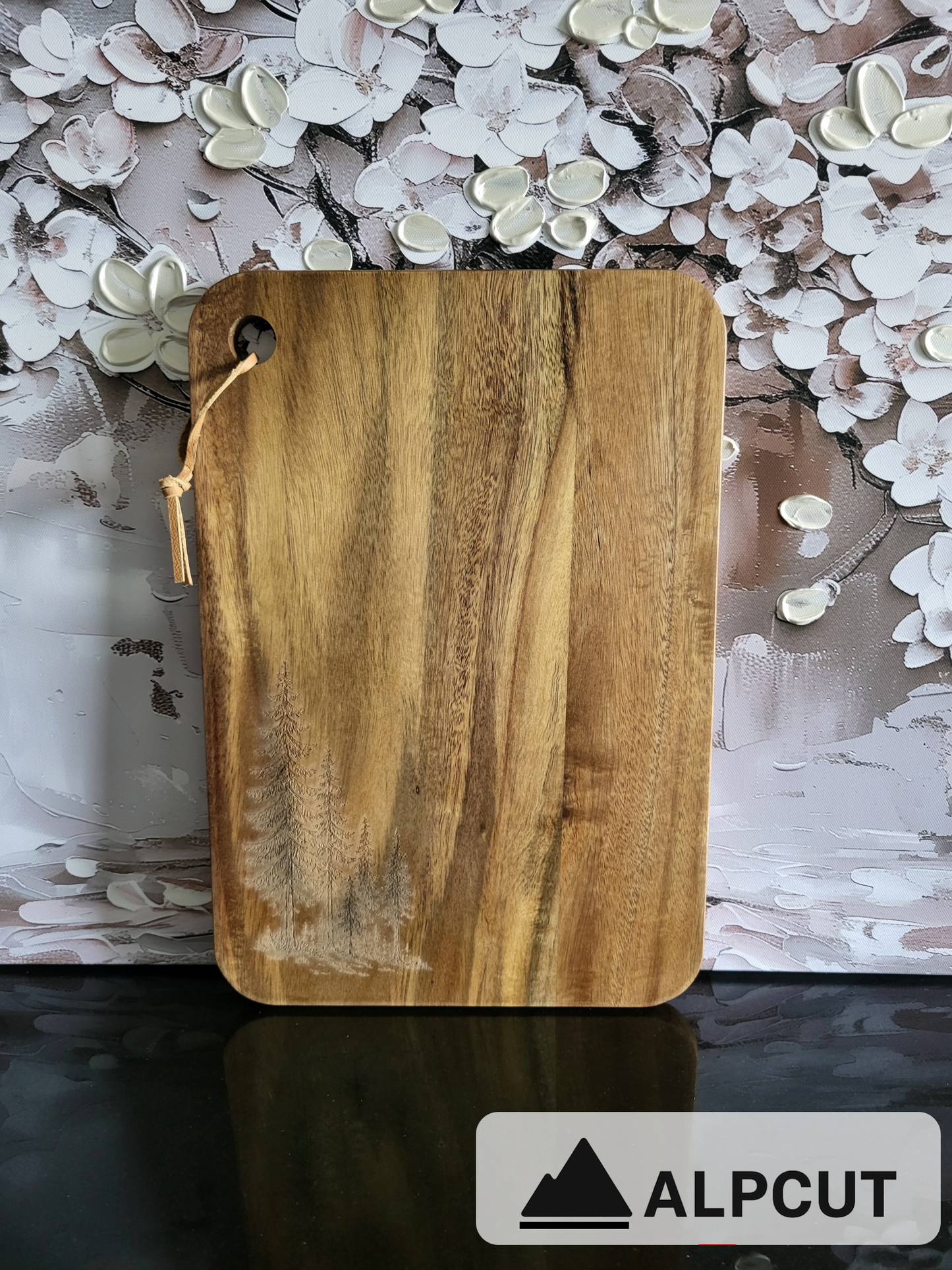 „Schneidebrett aus Akazienholz mit Gravur von Tannenbäumen – handgefertigt von ALPCUT. Edles Naturholzbrett mit einzigartiger Maserung und rustikalem Waldmotiv. Vielseitig einsetzbar als Schneidebrett, Käsebrett oder Servierbrett. Nachhaltig produziert und ideal als Geschenk für Naturliebhaber, Outdoor-Fans und Freunde der Schweizer Handwerkskunst.“