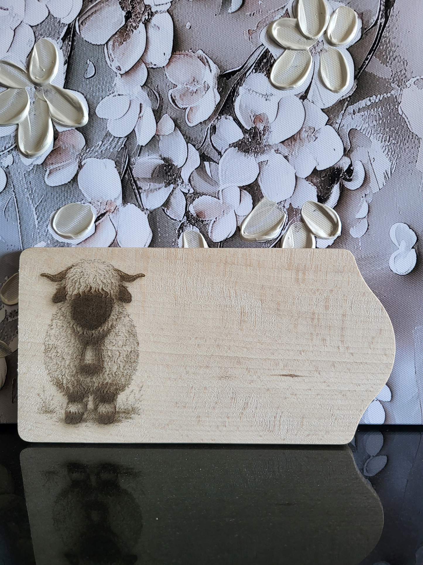 Frühstücksbrett aus Buchenholz mit Schwarznasenschaf-Motiv. Das Brett ist auf der rechten Seite abgerundet und zeigt eine detaillierte Gravur eines Walliser Schwarznasenschafs, das eine Glocke trägt. Ideal für Kinder und Schaf-Liebhaber und als originelles Küchenaccessoire.