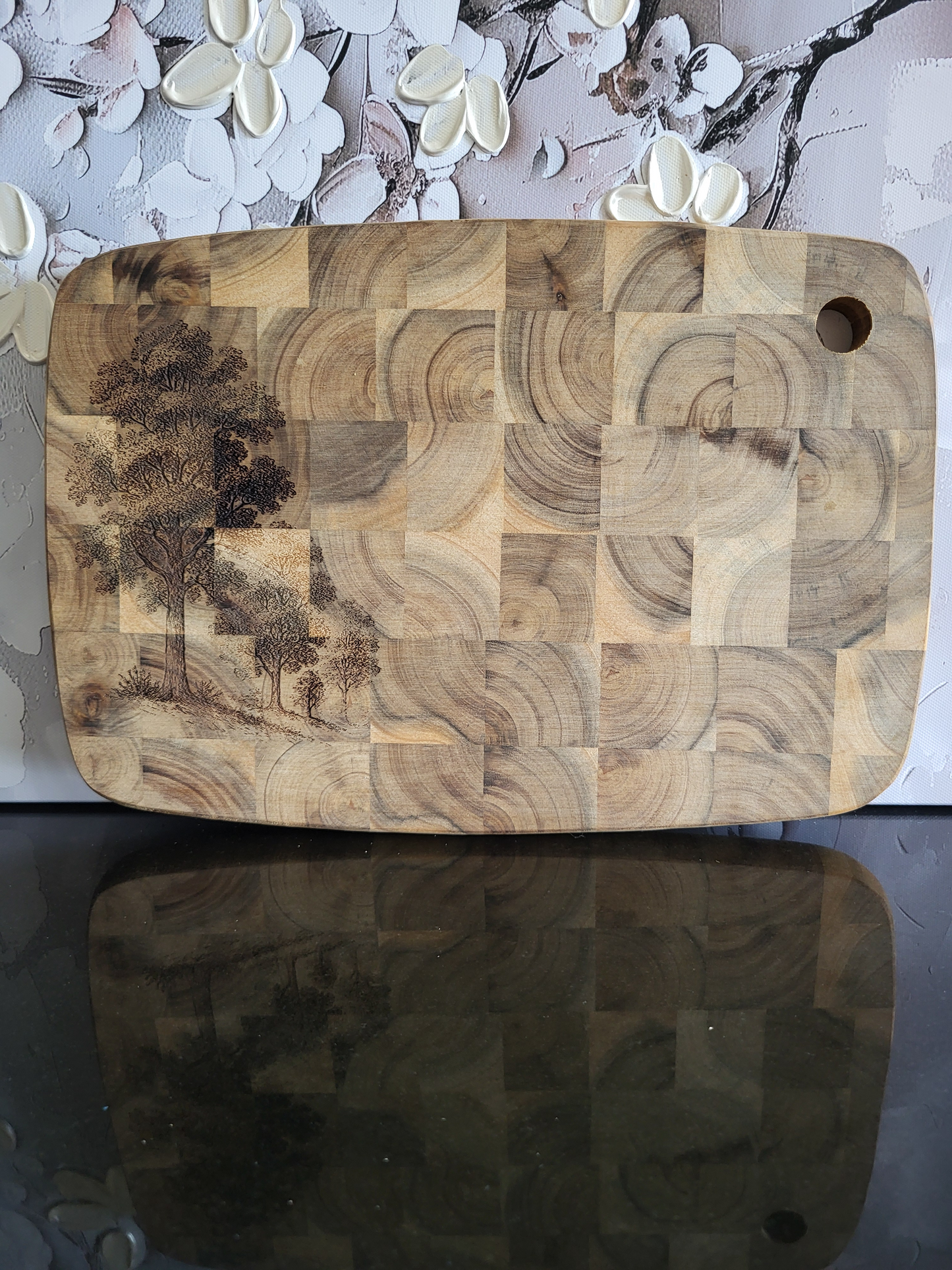 Rechteckiges Schneidebrett aus Akazienholz in Stirnholzoptik mit markanter Blockmusterung. Auf der linken Seite ist eine feine Gravur von Bäumen eingearbeitet, die dem massiven Holzbrett eine natürliche, künstlerische Note verleiht. Hochwertiges, handgefertigtes Küchen- und Servierbrett von ALPCUT – robust, langlebig und ideal zum Schneiden, Servieren oder stilvollen Präsentieren.