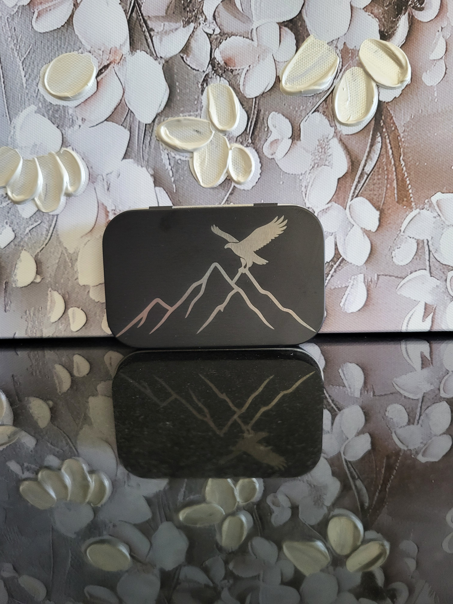 Gravierte Metalldose mit Adler-Motiv und Berglandschaft. Diese schwarze Aufbewahrungsbox zeigt einen majestätischen Adler, der über schroffe Berge fliegt. Ideal als Geschenk für Wanderer, Bergfreunde und Liebhaber von alpinen Motiven. Perfekt zur Aufbewahrung von Kleinteilen, Pillen oder als Schmuckdose.