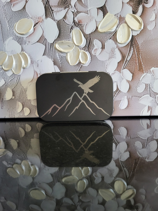 Gravierte Metalldose mit Adler-Motiv und Berglandschaft. Diese schwarze Aufbewahrungsbox zeigt einen majestätischen Adler, der über schroffe Berge fliegt. Ideal als Geschenk für Wanderer, Bergfreunde und Liebhaber von alpinen Motiven. Perfekt zur Aufbewahrung von Kleinteilen, Pillen oder als Schmuckdose.