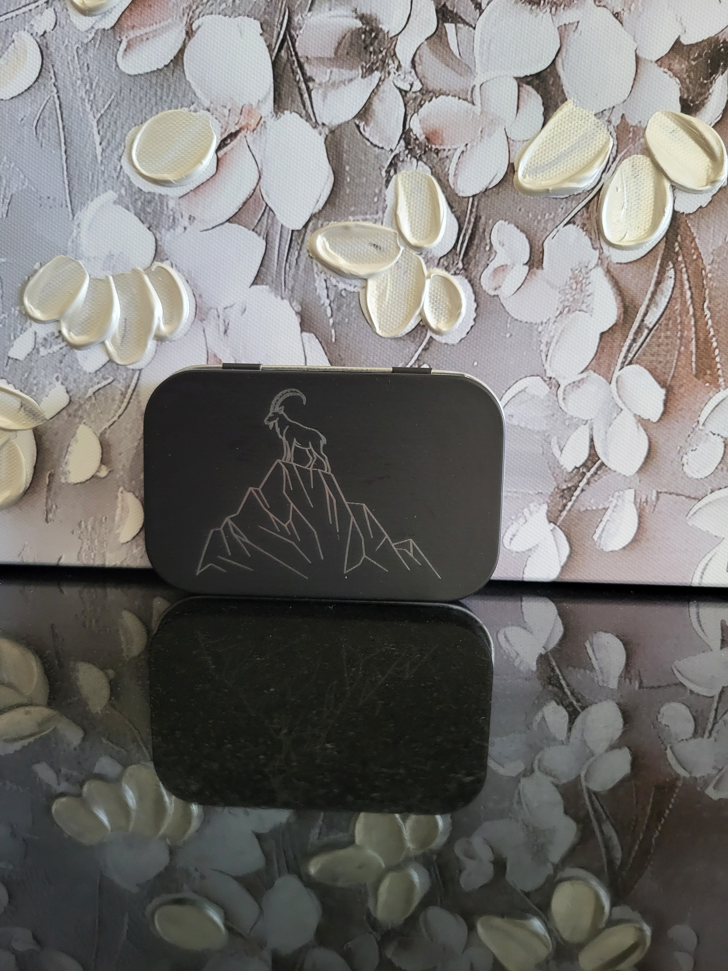 Gravierte Metalldose mit Berg- und Steinbock-Motiv. Diese schwarze Aufbewahrungsbox zeigt einen stolzen Steinbock auf einem Felsen. Ideal als Geschenk für Wanderer, Bergsteiger oder Naturliebhaber. Perfekt zur Aufbewahrung von Kleinteilen, Pillen oder als Schmuckdose.