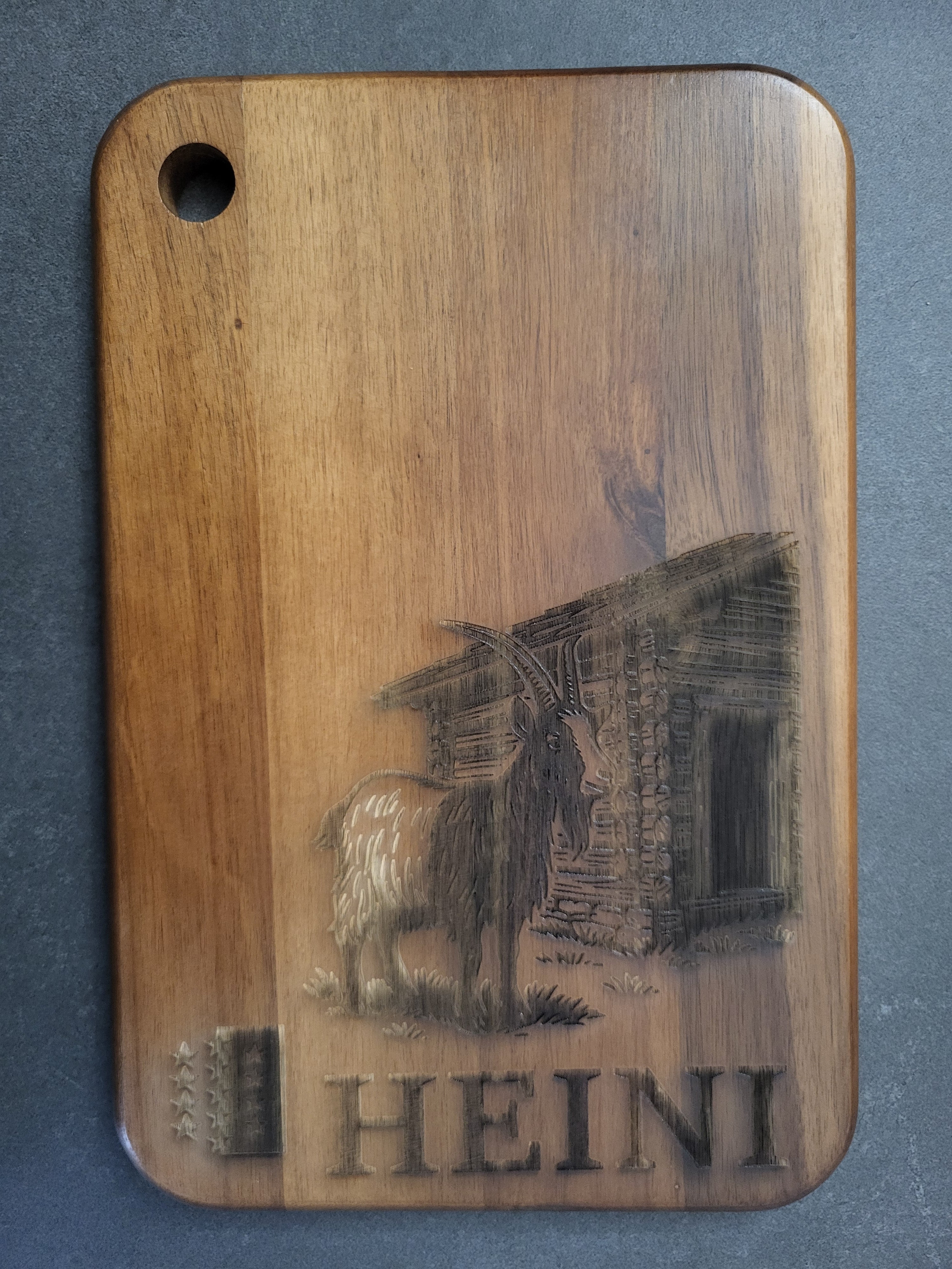 Individuelles Schneidebrett aus Akazienholz mit Gravur – Schweizer Schwarzhalsziege vor Alphütte und personalisierter Namensgravur „Heini“ – hochwertiges, handgefertigtes Holzbrett als Geschenkidee oder Deko – rustikales Unikat aus Massivholz