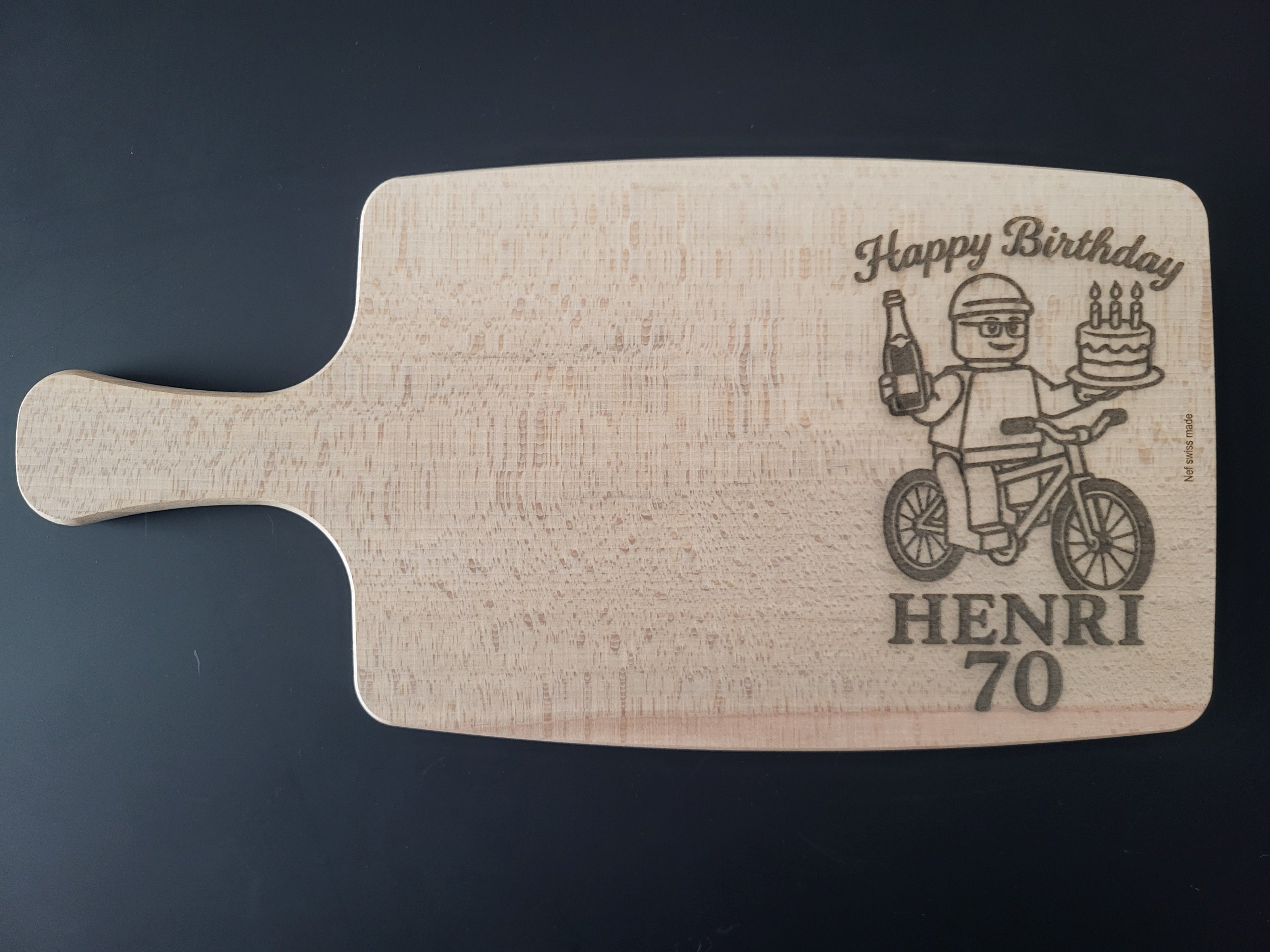 Personalisiertes Schneidebrett aus Holz zum Geburtstag – graviert mit Lego-inspiriertem Männchen auf Fahrrad, Kuchen und Getränk – mit Wunschtext „Happy Birthday“, Name und Alter – individuelles Geschenkbrett aus Holz, Swiss Made