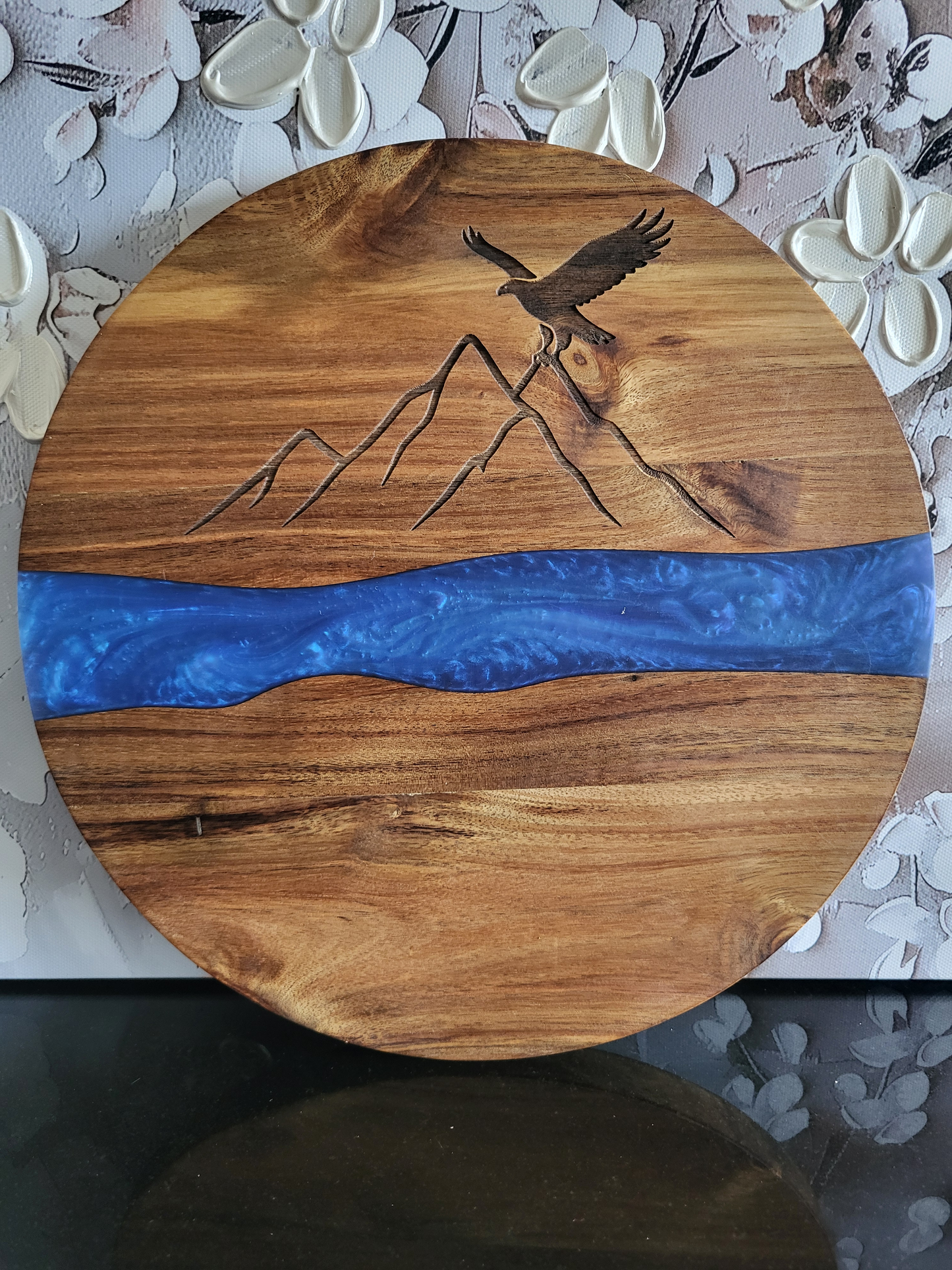 Rundes Schneidebrett aus Akazienholz mit blauer Epoxidharz-Einlage, dekorativer Gravur eines Adlers über Berglinien, handgefertigt von ALPCUT – edles Servier- und Dekobrett, ideal als Geschenk oder Küchenaccessoire.