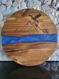 Rundes Schneidebrett aus Akazienholz mit blauer Epoxidharz-Einlage, dekorativer Gravur eines Adlers über Berglinien, handgefertigt von ALPCUT – edles Servier- und Dekobrett, ideal als Geschenk oder Küchenaccessoire.