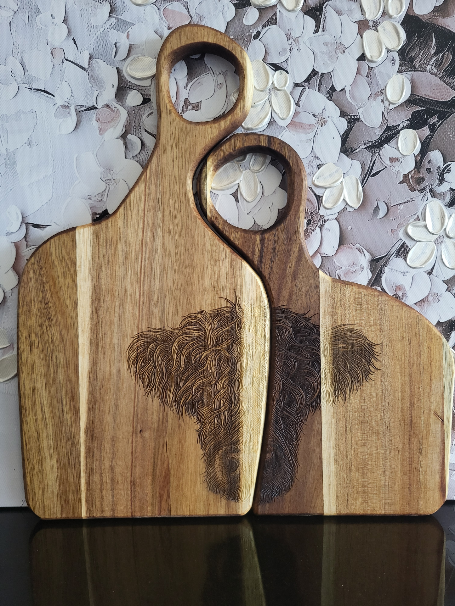 Zwei rechteckige Schneide- und Servierbretter aus Akazienholz mit rundem Griffloch, verziert mit detailreicher Gravur eines Highland-Rinds. Handgefertigte Holzbrettchen von ALPCUT, naturbelassen und einzigartig gemasert – ideal zum Servieren, Schneiden oder als rustikales Geschenk für Tier- und Naturfreunde.