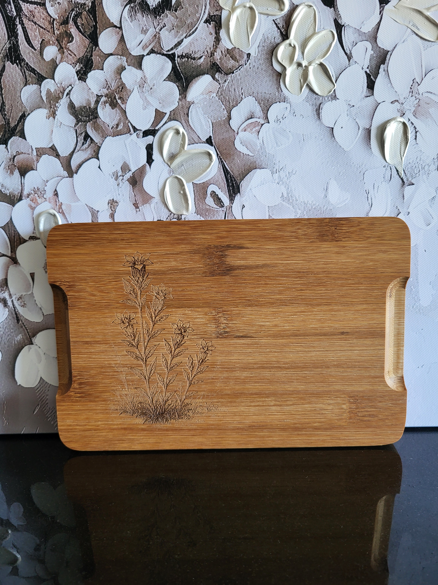 Wendenbares Schneidebrett aus Bambus mit Blumen-Gravur. Die Vorderseite ziert ein kunstvolles Motiv, während die Rückseite eine praktische Saftrinne hat. Ideal als Küchenbrett, Servierplatte oder Schneideunterlage. Perfekt für die Zubereitung von Speisen, die viel Saft abgeben.