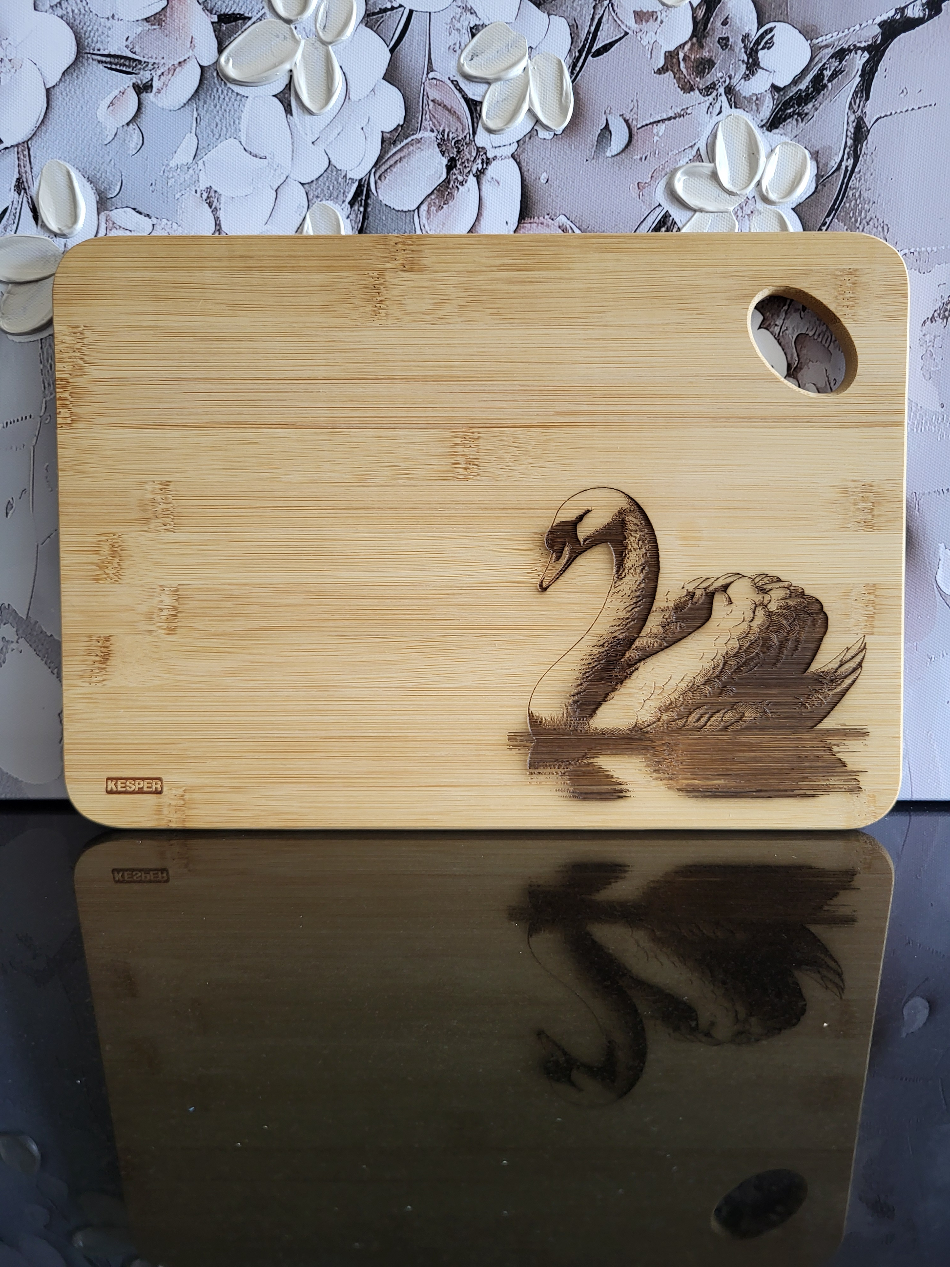 Rechteckiges Schneidebrett aus hellem Bambusholz mit abgerundeten Ecken und seitlicher Grifföffnung. Auf der Vorderseite ist eine detailreiche Gravur eines schwimmenden Schwans zu sehen, der elegant über die Wasseroberfläche gleitet. Das natürliche Bambus-Muster harmoniert mit der filigranen Gravur und verleiht dem Brett eine edle, zeitlose Optik. Ein stilvolles Küchenbrett von ALPCUT – nachhaltig, dekorativ und vielseitig einsetzbar als Schneide- oder Servierbrett.