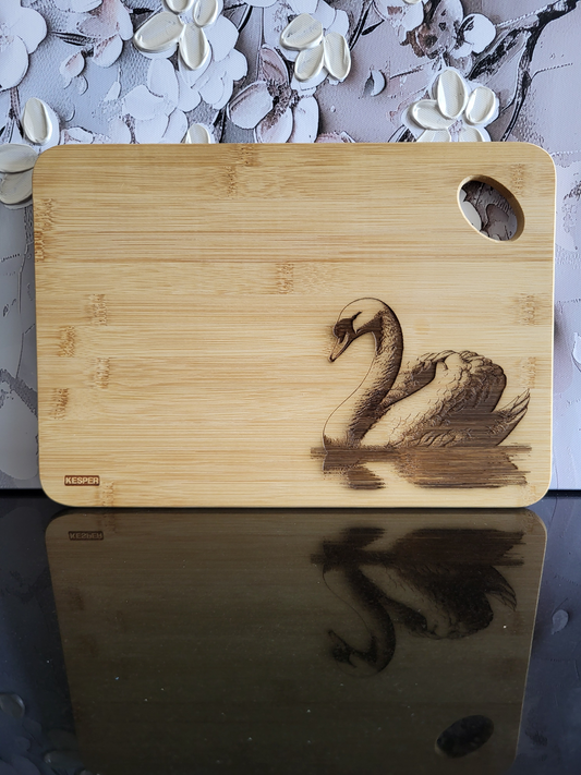 Rechteckiges Schneidebrett aus hellem Bambusholz mit abgerundeten Ecken und seitlicher Grifföffnung. Auf der Vorderseite ist eine detailreiche Gravur eines schwimmenden Schwans zu sehen, der elegant über die Wasseroberfläche gleitet. Das natürliche Bambus-Muster harmoniert mit der filigranen Gravur und verleiht dem Brett eine edle, zeitlose Optik. Ein stilvolles Küchenbrett von ALPCUT – nachhaltig, dekorativ und vielseitig einsetzbar als Schneide- oder Servierbrett.