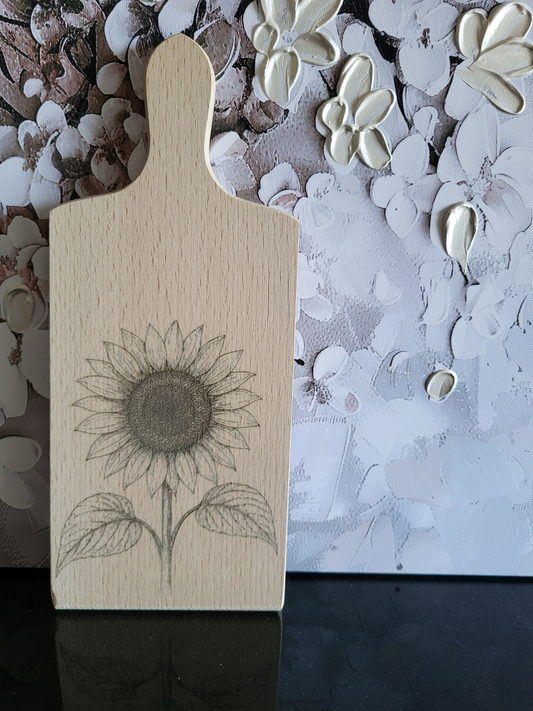 Schneide- oder Servierbrett aus hellem Holz, graviert mit einer großen Sonnenblume. Dieses Blumen-Motiv ist ideal als Geschenk für Gartenfreunde, Naturliebhaber oder als stilvolle Küchen- und Esszimmerdekoration.
