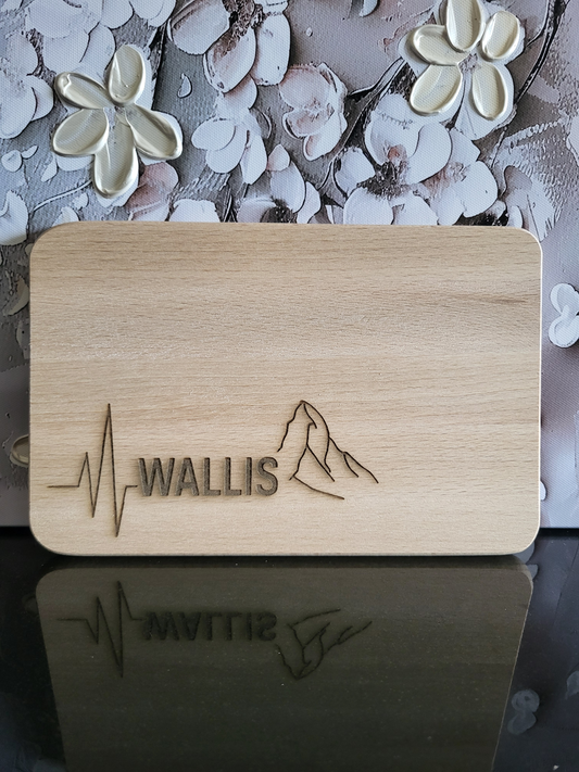 Rechteckiges Schneidebrett aus hellem Buchenholz mit abgerundeten Ecken. Auf der Vorderseite ist eine feine Gravur angebracht: Links ein stilisierter Herzschlag, daneben der Schriftzug „WALLIS“ in Großbuchstaben. Rechts davon ein minimalistisches Linienmotiv des Matterhorns, das als Symbol für das Wallis steht. Das Brett vereint schlichte Eleganz mit regionalem Bezug und eignet sich sowohl als Küchenutensil als auch als dekoratives Geschenk mit alpinem Charakter.