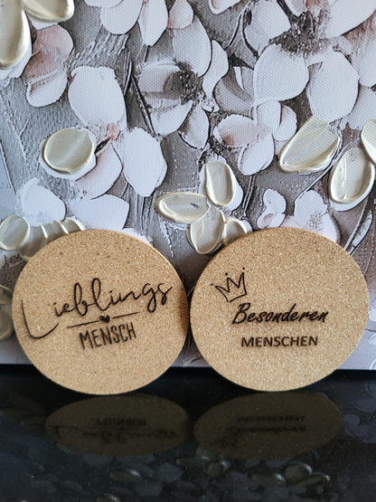 Set aus fünf Korkuntersetzern für Apéro oder Cocktails. Die gravierten Untersetzer zeigen verschiedene Motive wie einen Bären mit Brille, einen Bären im Ringelshirt und ein Martini-Glas. Zwei weitere Untersetzer sind mit den Sprüchen "Lieblingsmensch" und "Besonderen MENSCHEN" beschriftet. Perfekt als Geschenkset für Liebhaber von stilvollem Bar-Zubehör oder als originelles Geschenk für Freunde und Familie.